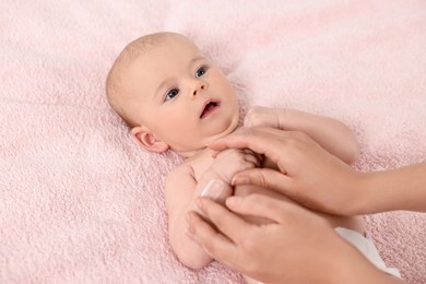 Woman applying body cream onto baby`s skin on bed, closeup