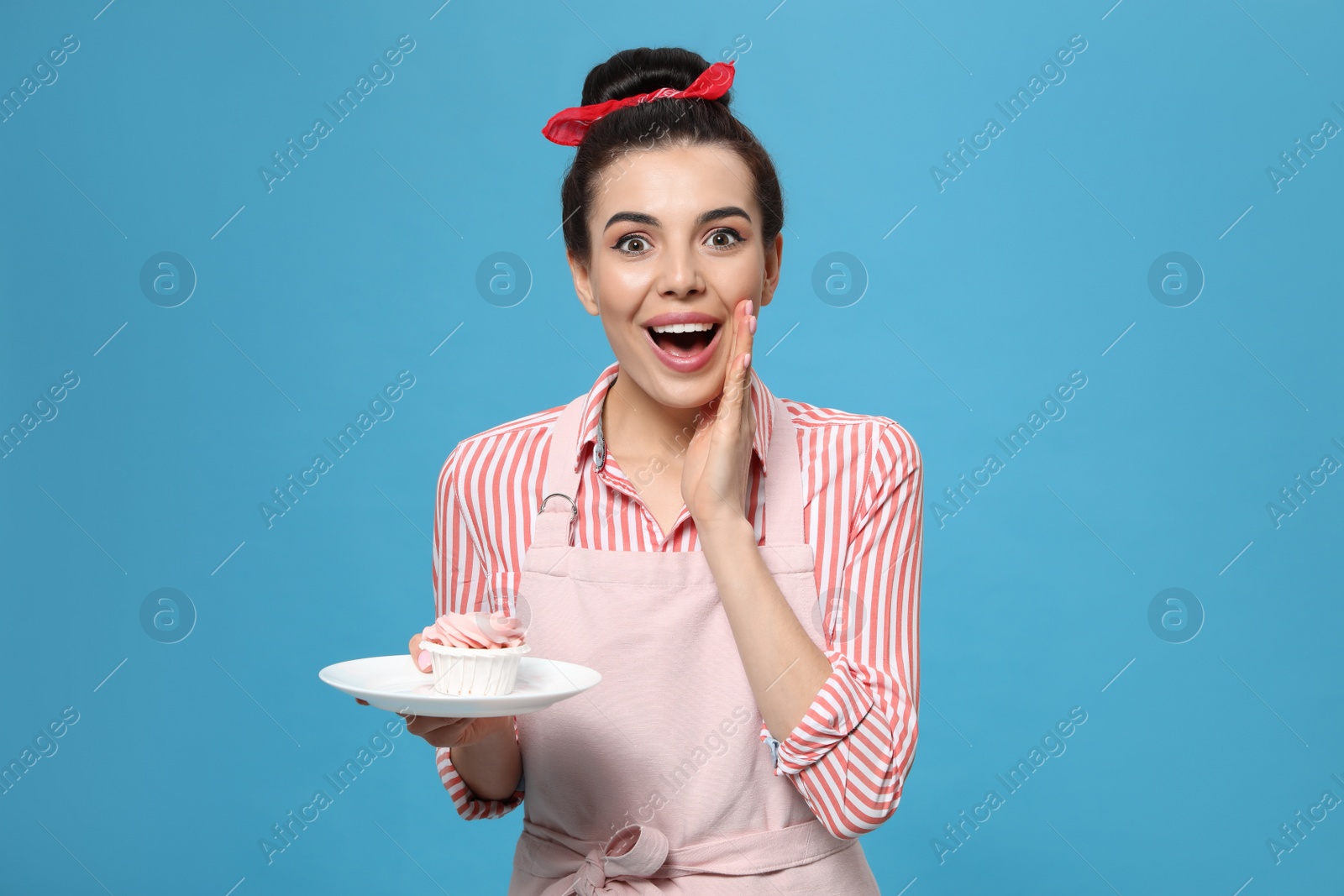 Photo of Young housewife with tasty cupcake on light blue background