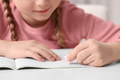 Photo of Girl using eraser at white desk, closeup