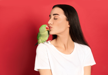 Young woman with Alexandrine parakeet on red background. Cute pet