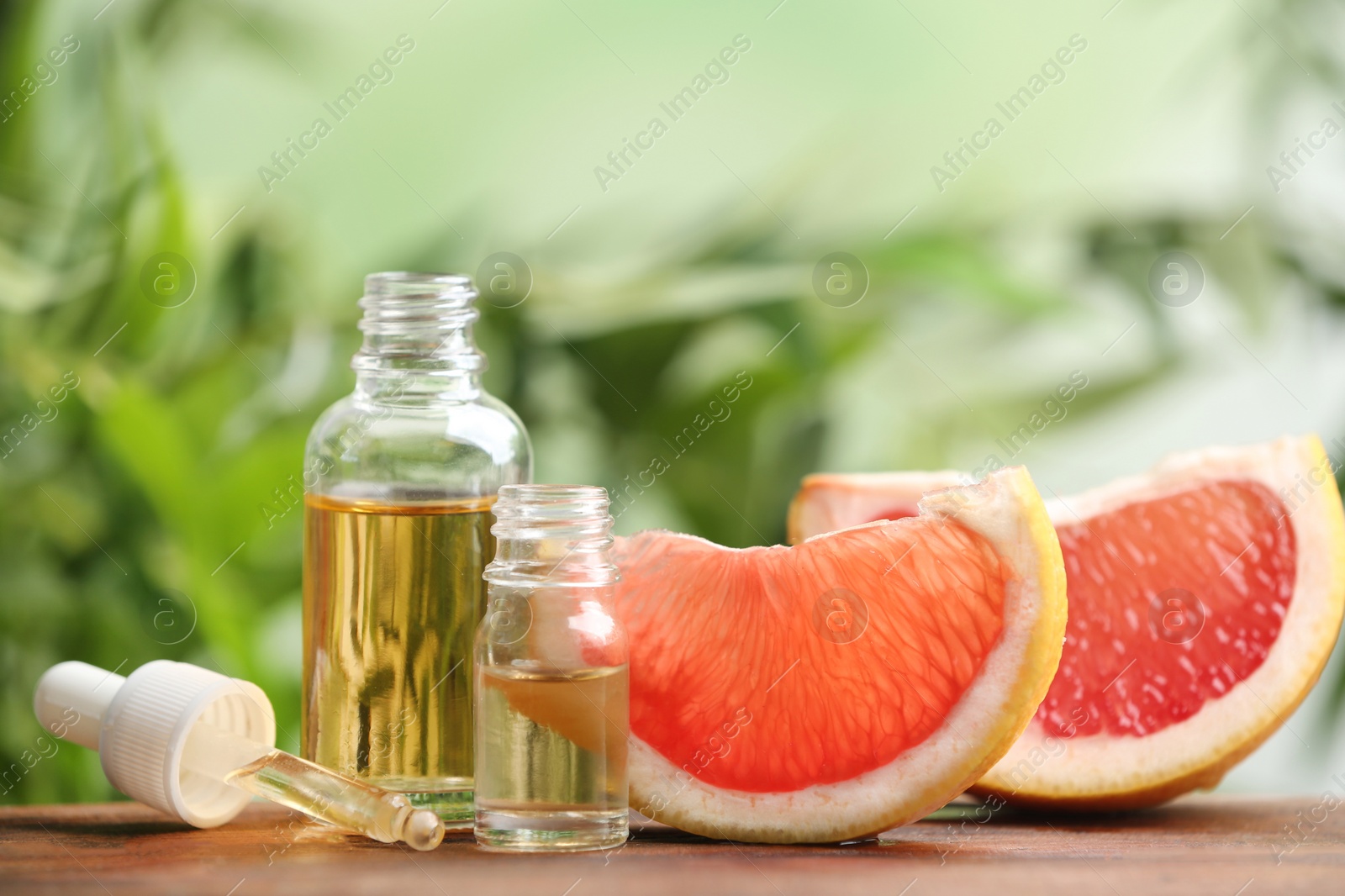 Photo of Bottles of essential oil and grapefruit slices on table against blurred background