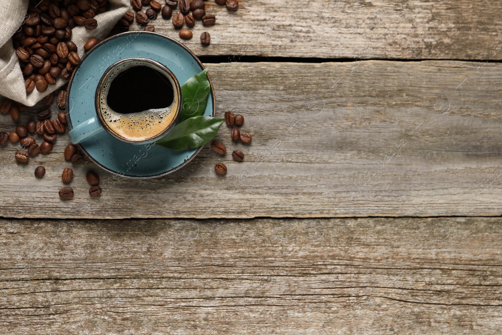 Photo of Cup of aromatic hot coffee and beans on wooden table, flat lay. Space for text