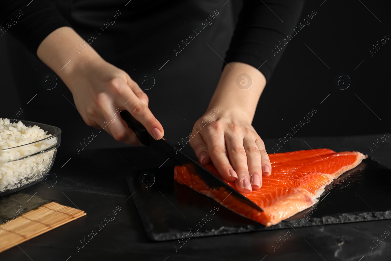 Photo of Chef cutting salmon for sushi at dark table, closeup