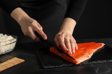 Photo of Chef cutting salmon for sushi at dark table, closeup