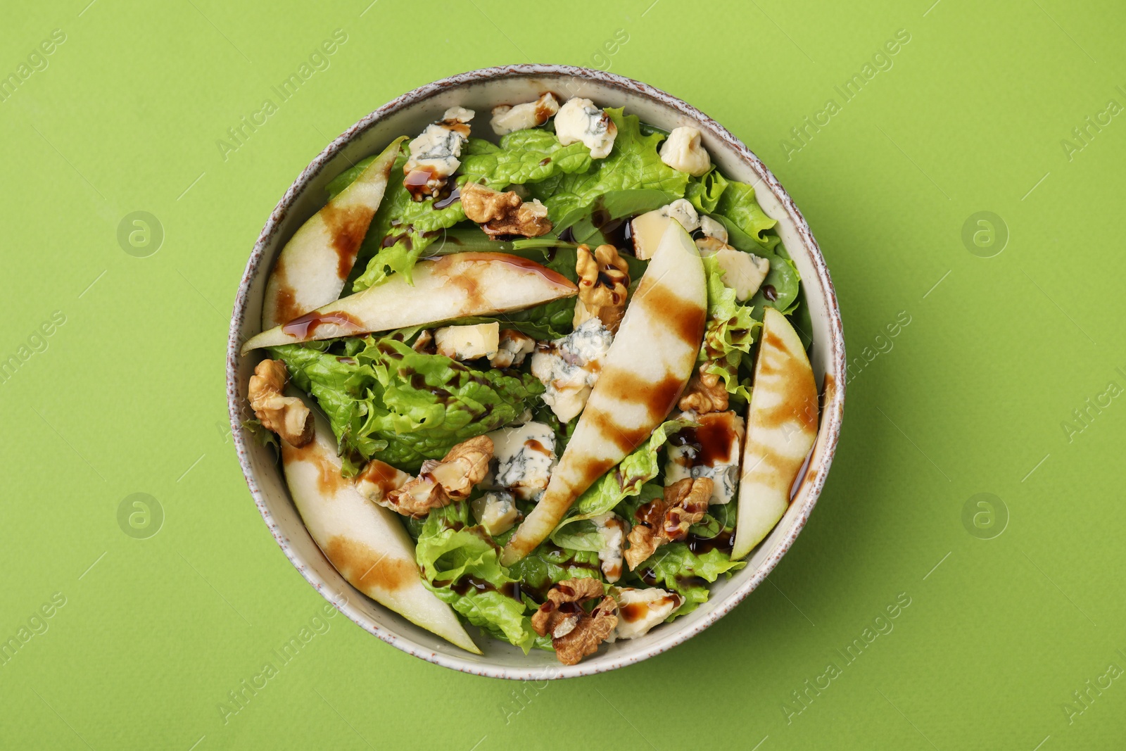 Photo of Delicious pear salad with sauce in bowl on green background, top view