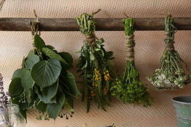 Photo of Bunches of different beautiful dried flowers hanging on wooden stick near beige wall