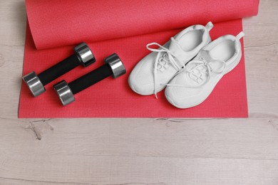 Photo of Dumbbells, sneakers and mat on wooden floor, above view