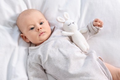 Photo of Cute little baby with toy lying on white sheets, top view