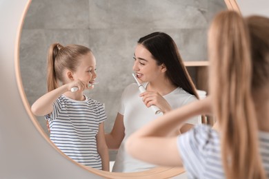 Mother and her daughter brushing teeth together near mirror in bathroom