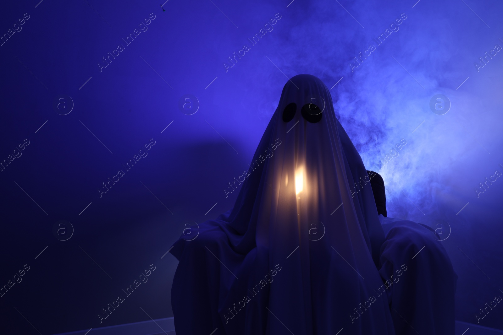 Photo of Creepy ghost. Woman covered with sheet in armchair in blue light, space for text