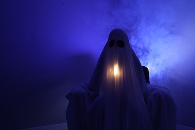 Creepy ghost. Woman covered with sheet in armchair in blue light, space for text