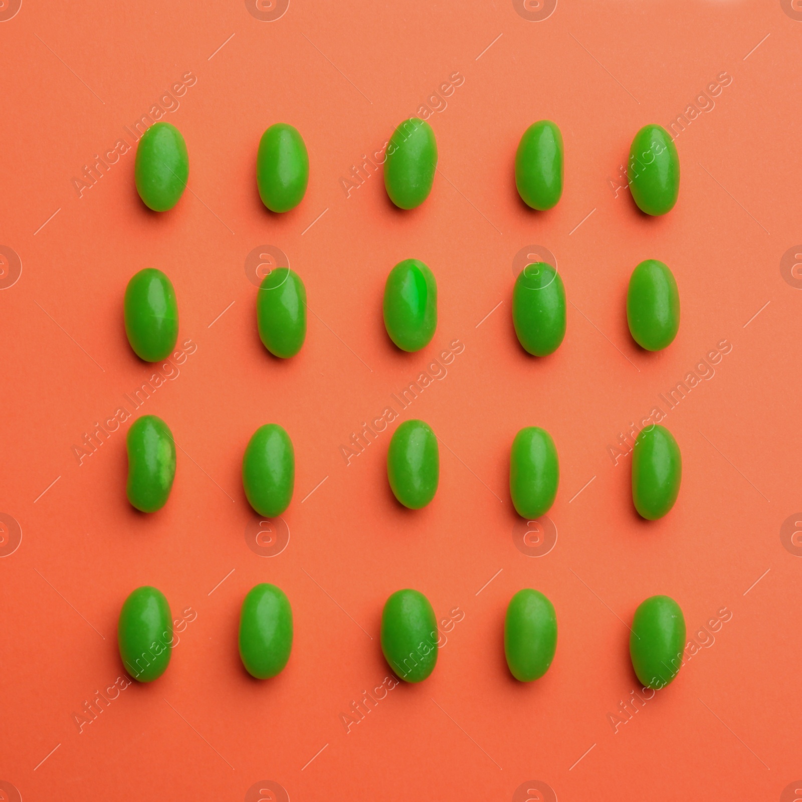 Photo of Green jelly beans on coral background, flat lay