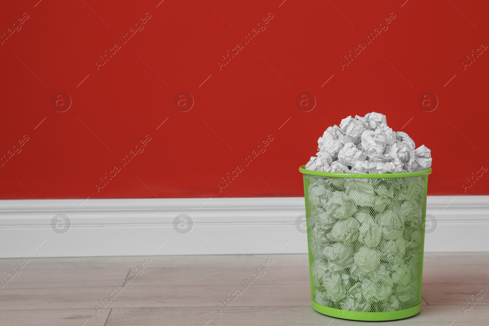 Photo of Metal bin with crumpled paper on floor against color wall. Space for text