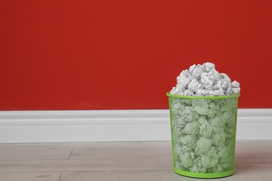 Metal bin with crumpled paper on floor against color wall. Space for text