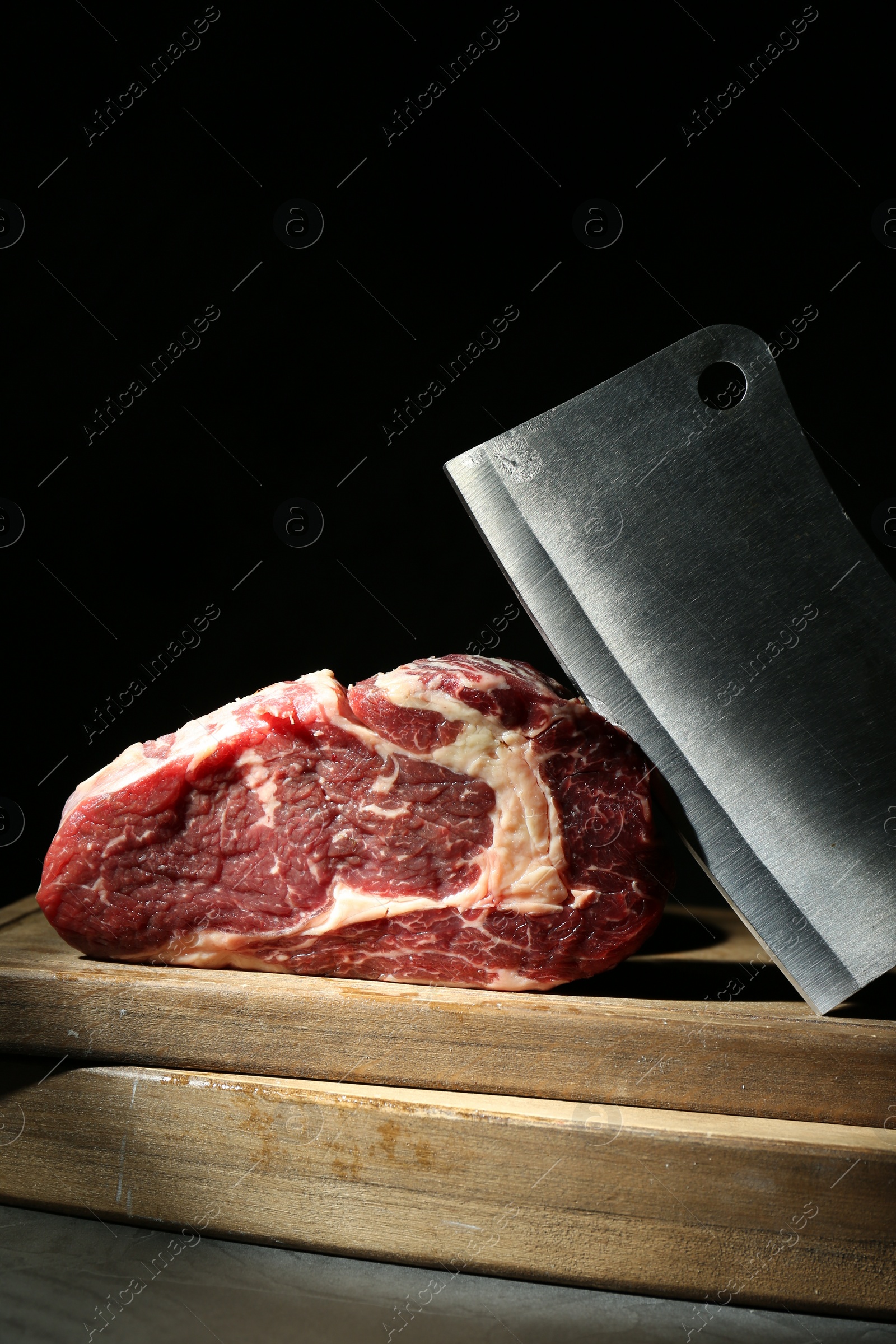 Photo of Piece of raw beef meat and knife on grey table against black background