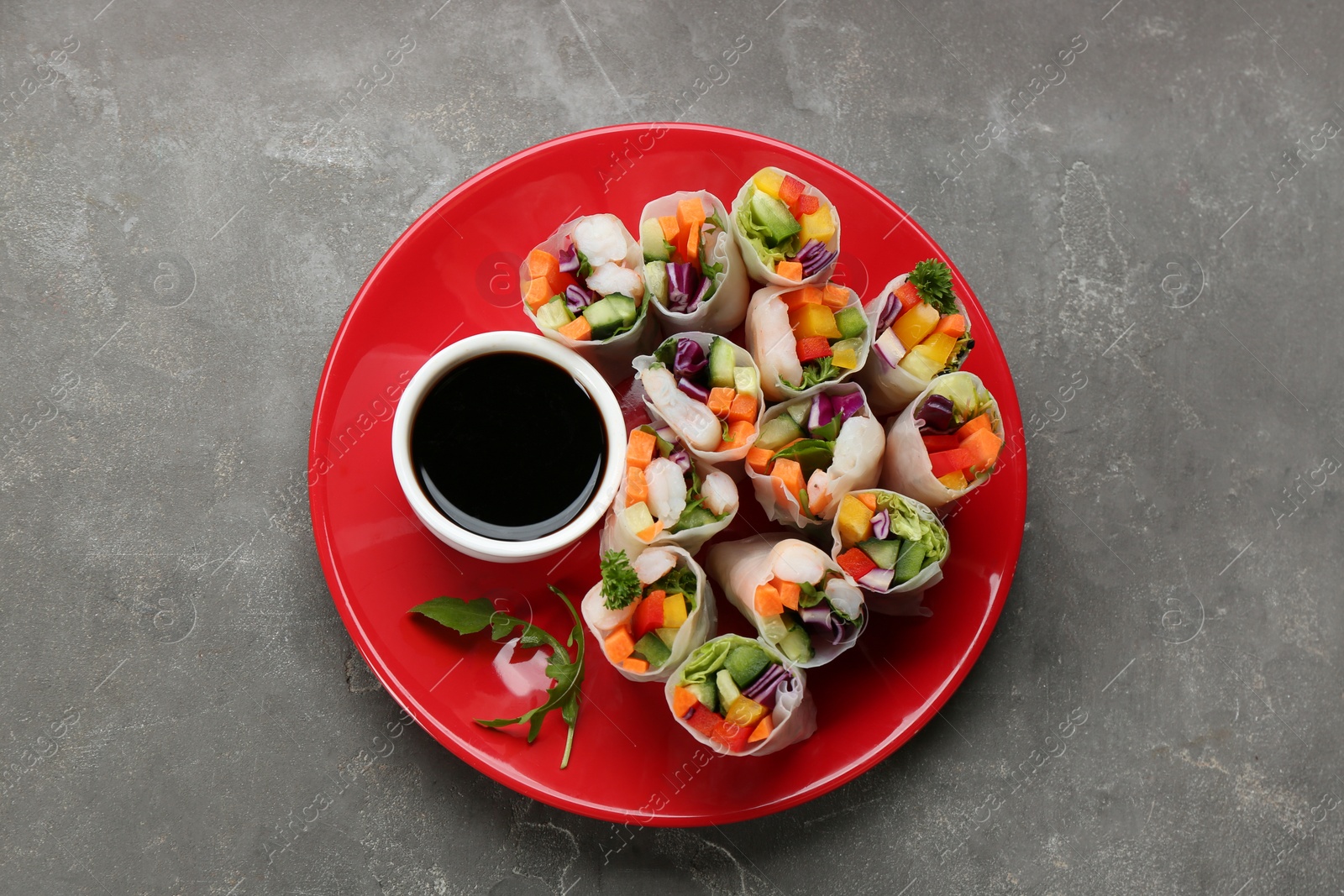 Photo of Delicious rolls wrapped in rice paper served on grey table, top view