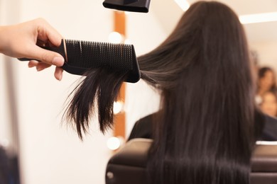 Photo of Hairdresser drying woman's hair in beauty salon, closeup