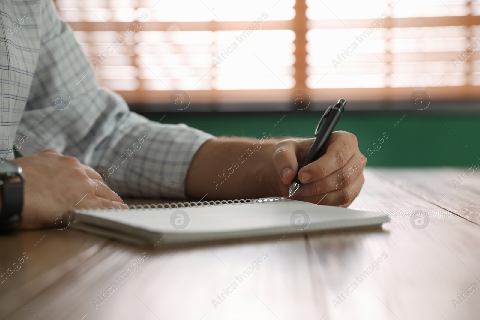 Photo of Left-handed man writing in notebook at wooden table indoors, closeup