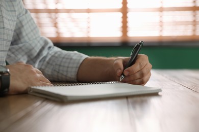Photo of Left-handed man writing in notebook at wooden table indoors, closeup