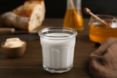 Glass with milk near butter, honey and bread on wooden table