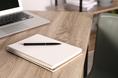 Photo of Notebook, pen and laptop on wooden table indoors