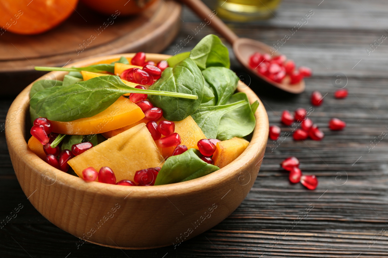 Photo of Delicious persimmon salad with pomegranate and spinach on wooden table