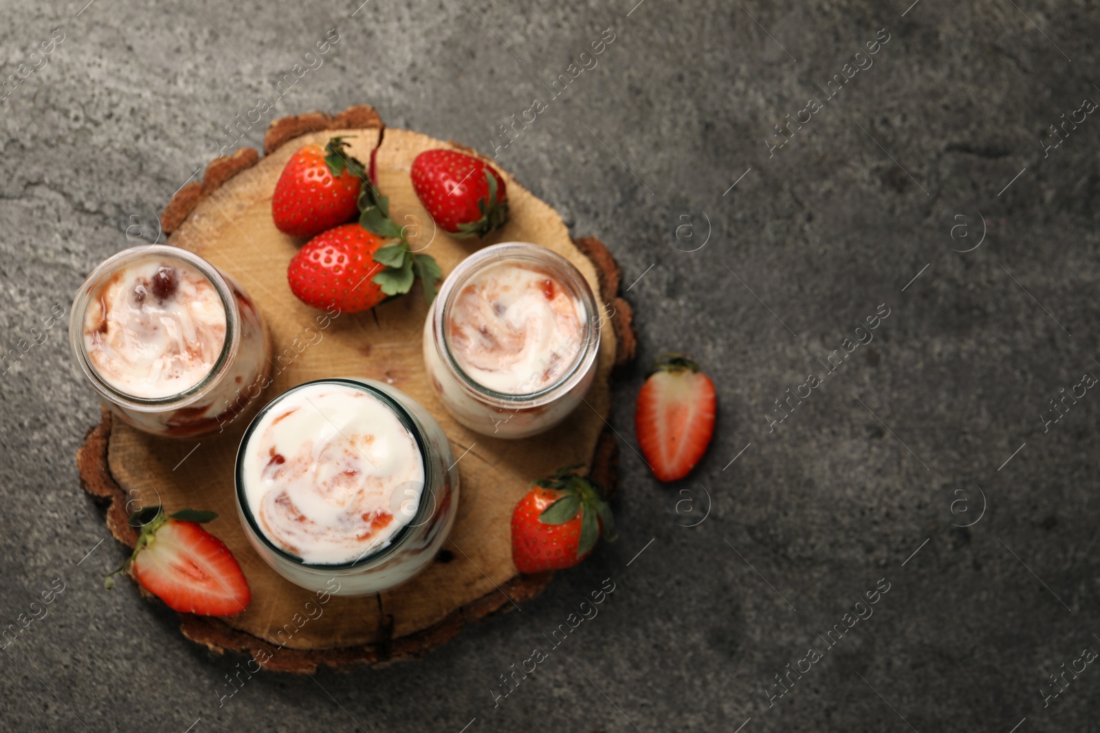 Photo of Tasty yoghurt with jam and strawberries on grey textured table, top view. Space for text