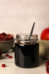 Photo of Glass jar of tasty pomegranate sauce on white marble table