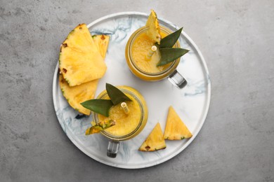 Photo of Tray with tasty pineapple smoothie and sliced fruit on grey table, top view