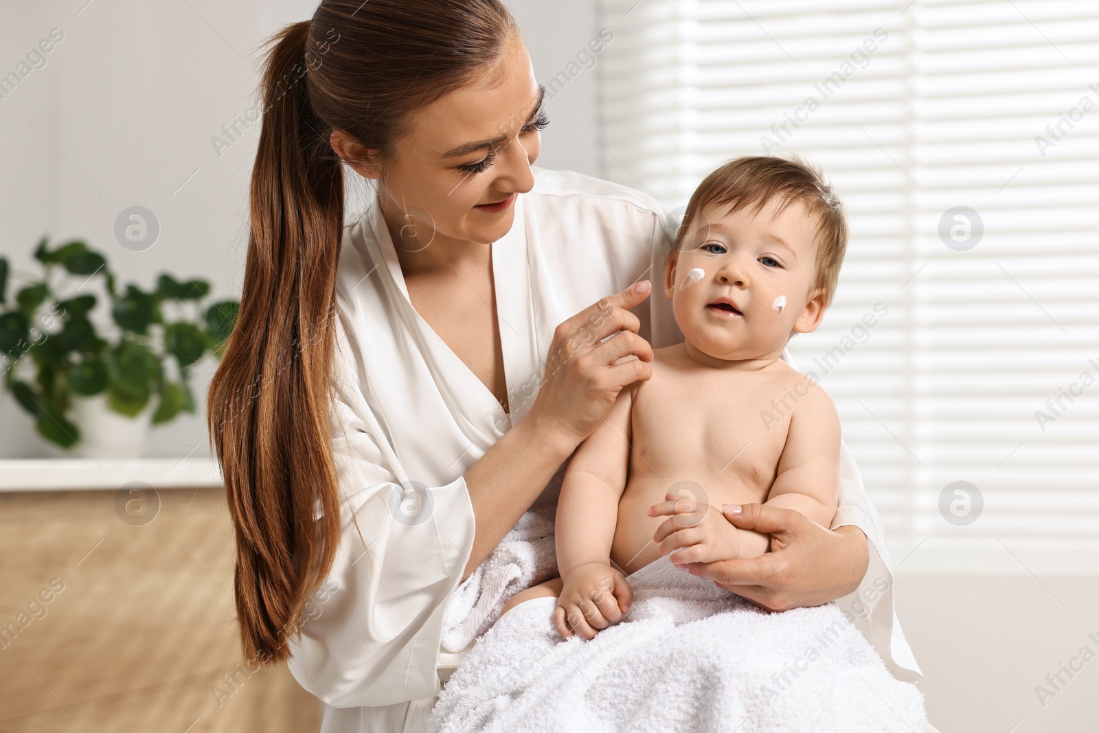 Photo of Happy mother applying body cream onto baby`s skin at home
