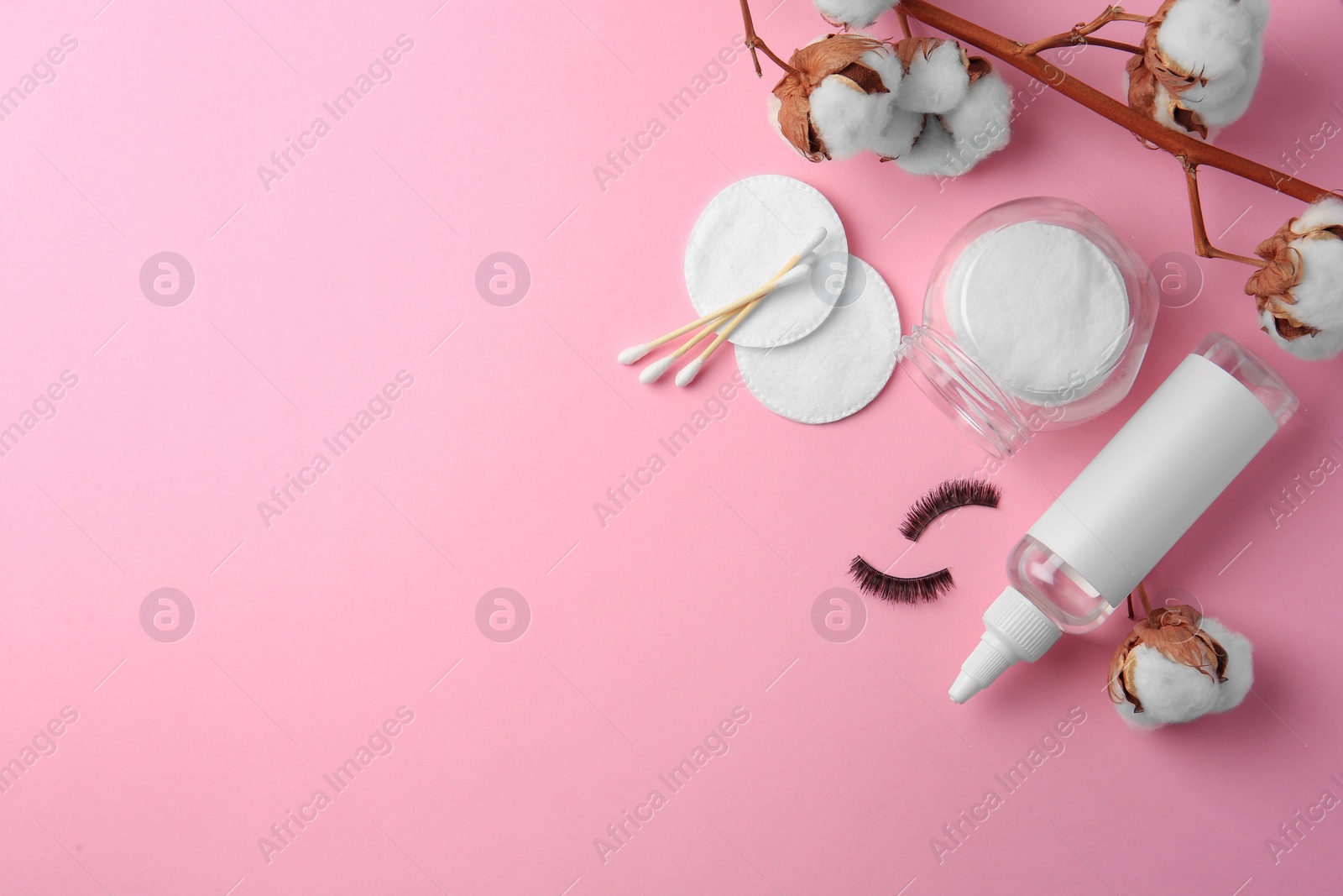 Photo of Bottle of makeup remover, cotton flowers, pads, swabs and false eyelashes on pink background, flat lay. Space for text