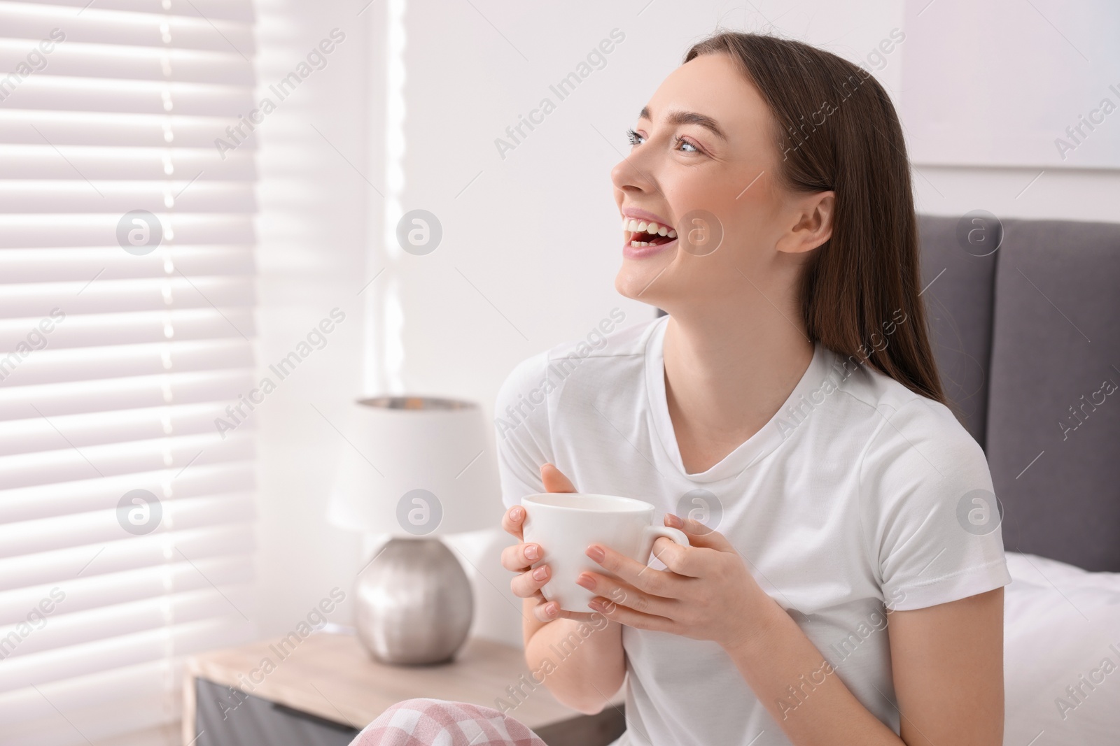 Photo of Beautiful woman with cup laughing in bedroom. Space for text