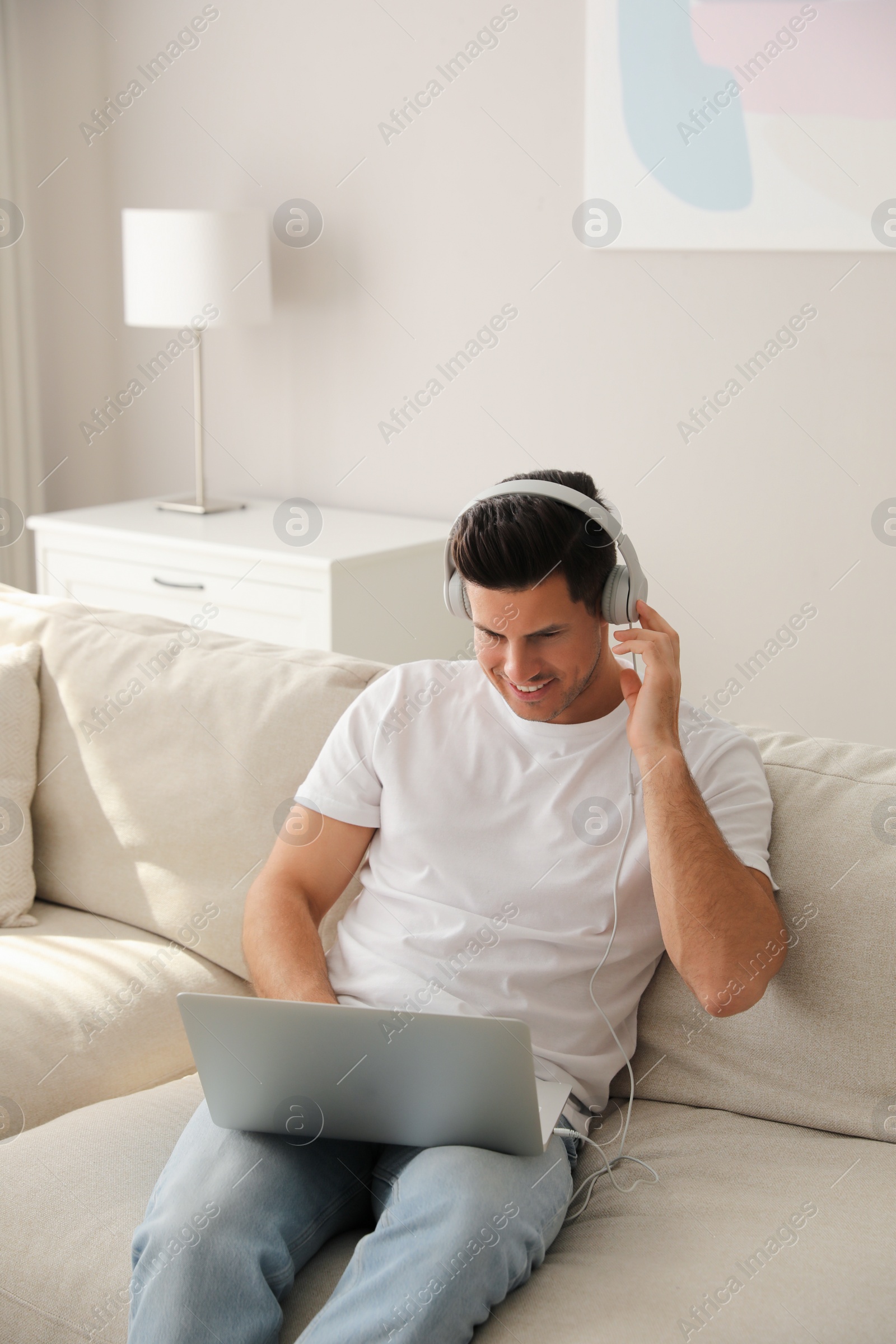 Photo of Man with laptop and headphones sitting on sofa at home