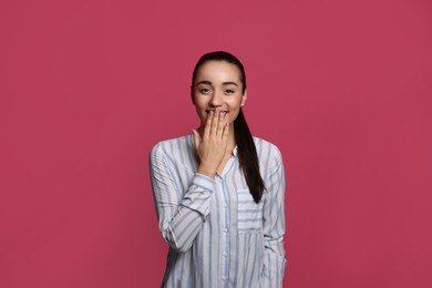 Beautiful young woman laughing on maroon background. Funny joke