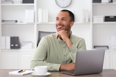 Photo of Handsome young man with laptop at table in office