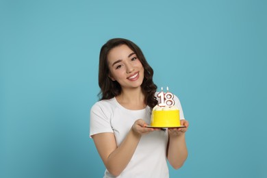 Coming of age party - 18th birthday. Woman holding delicious cake with number shaped candles on light blue background