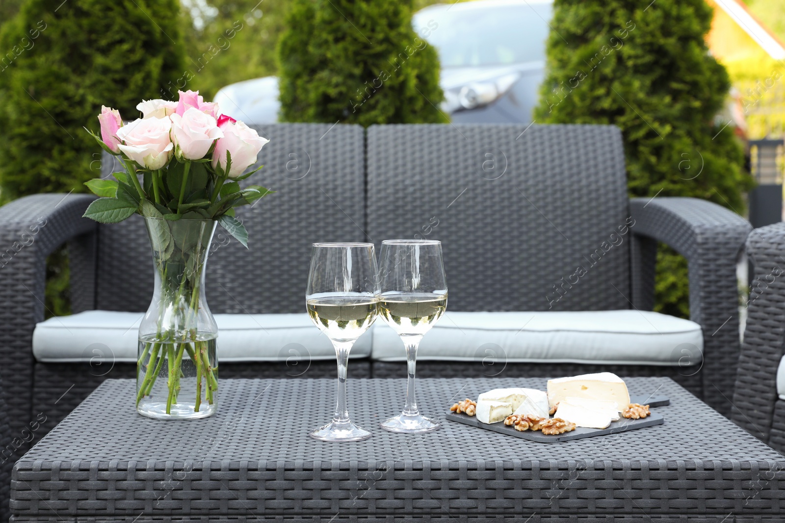 Photo of Vase with roses, glasses of wine and food on rattan table on outdoor terrace