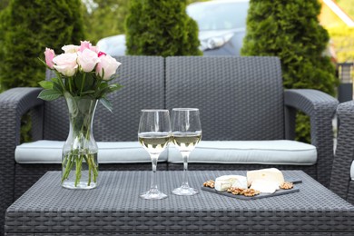 Vase with roses, glasses of wine and food on rattan table on outdoor terrace