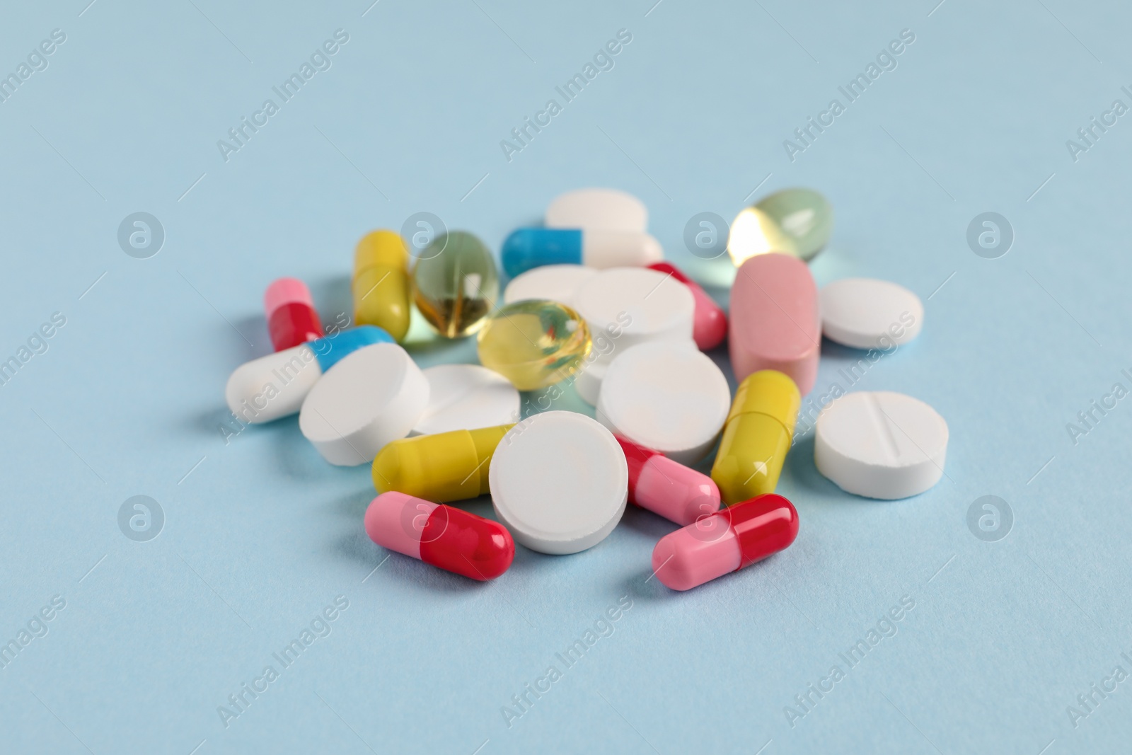 Photo of Pile of colorful pills on light blue background, closeup