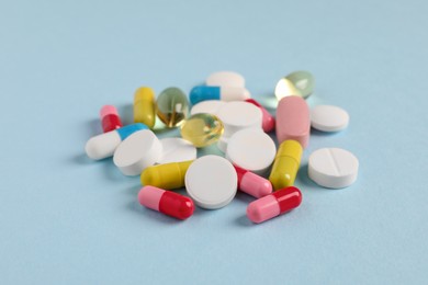 Pile of colorful pills on light blue background, closeup