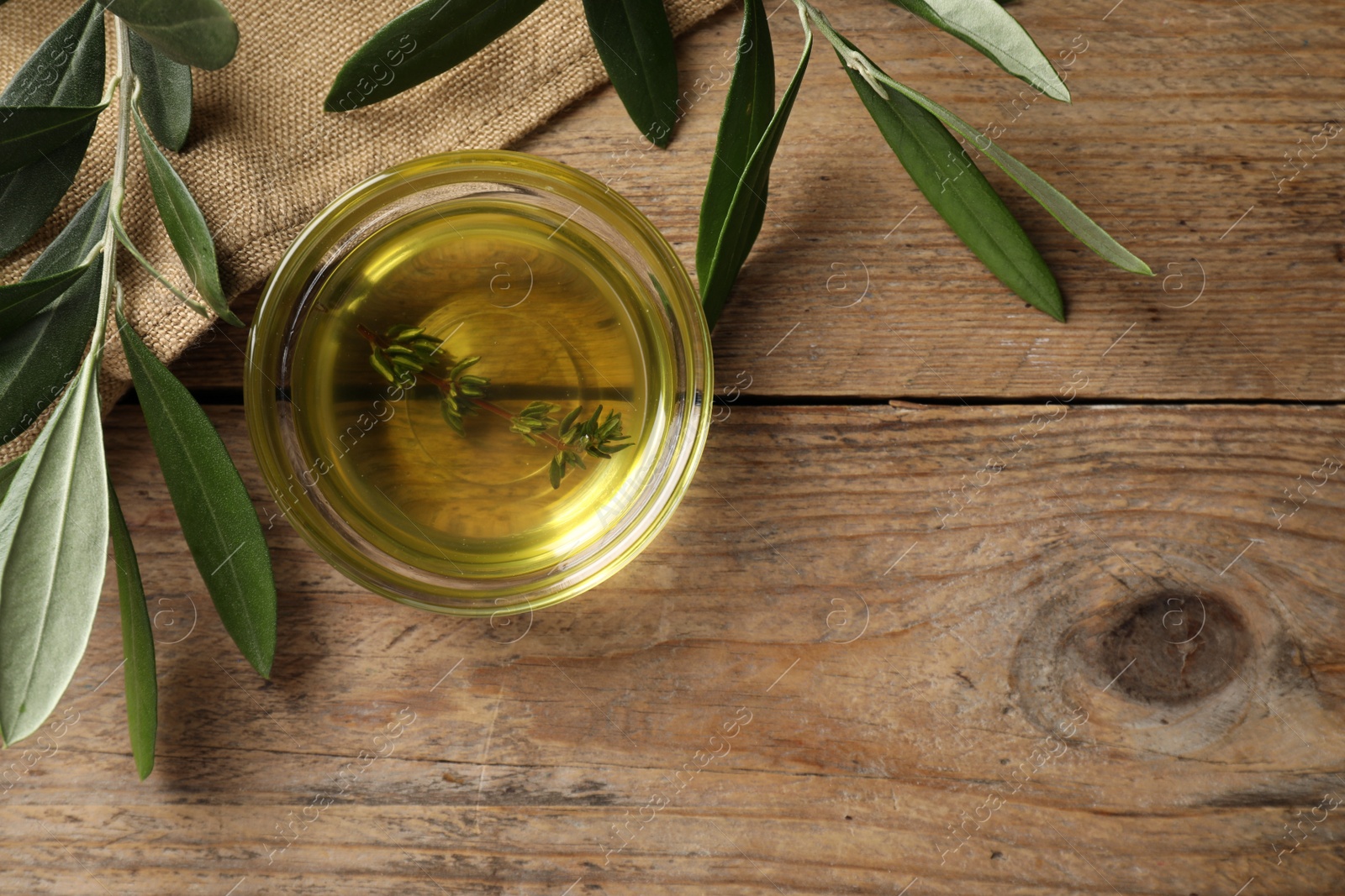 Photo of Bowl of olive oil with thyme on wooden table, flat lay. Space for text