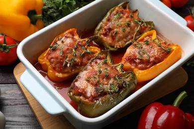 Photo of Tasty stuffed peppers in dish and ingredients on wooden table, closeup