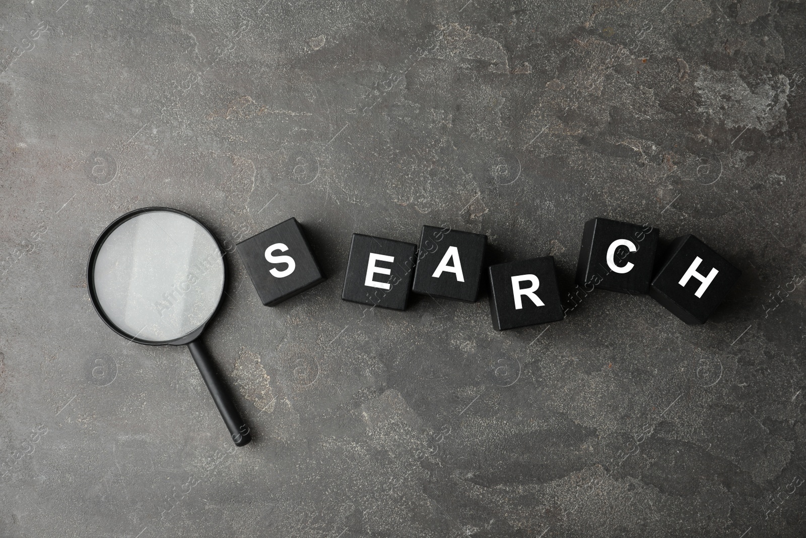 Photo of Word SEARCH made of black cubes and magnifier glass on grey stone background, flat lay. Find keywords concept