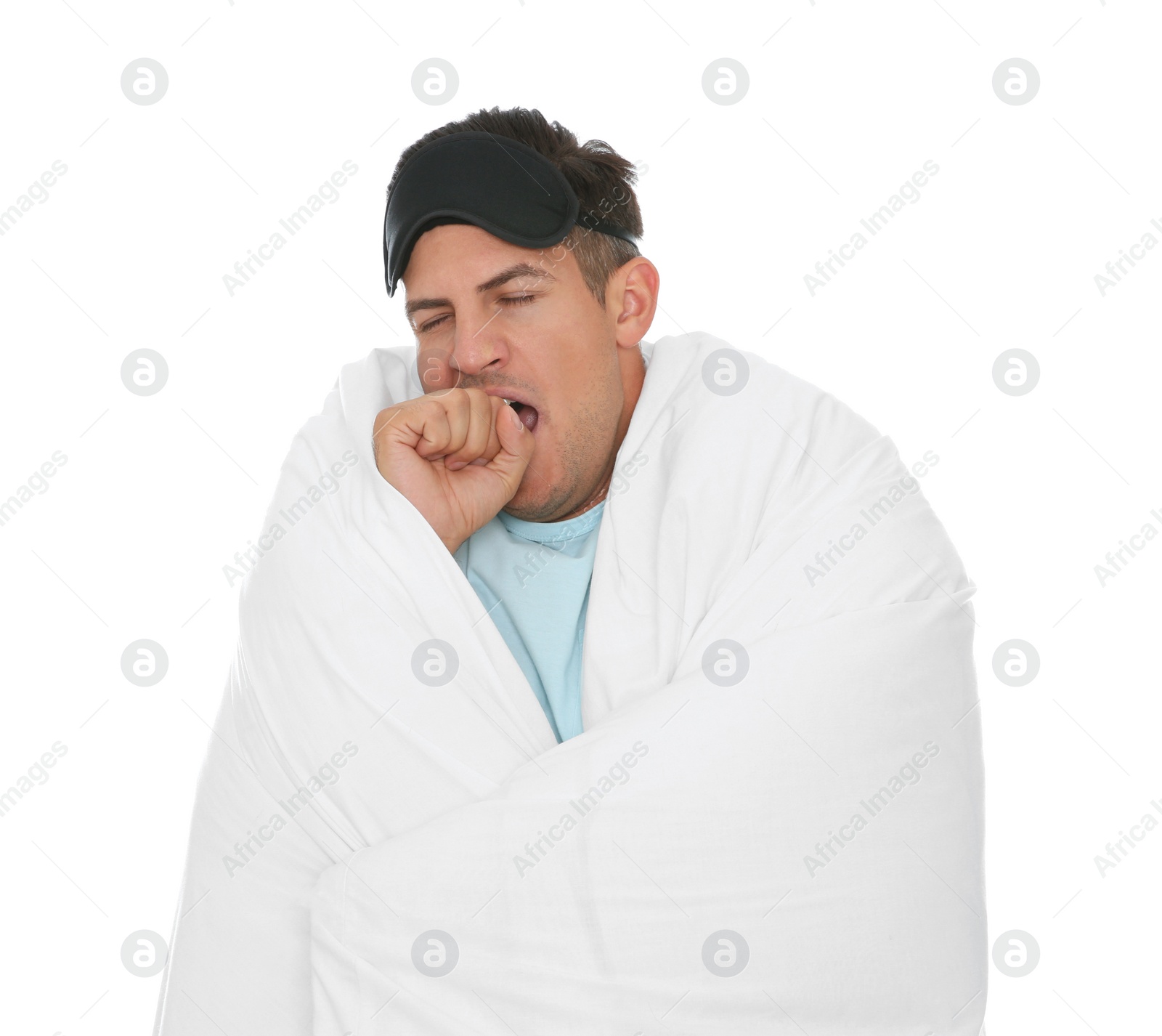 Photo of Man in sleeping mask wrapped with blanket yawning on white background