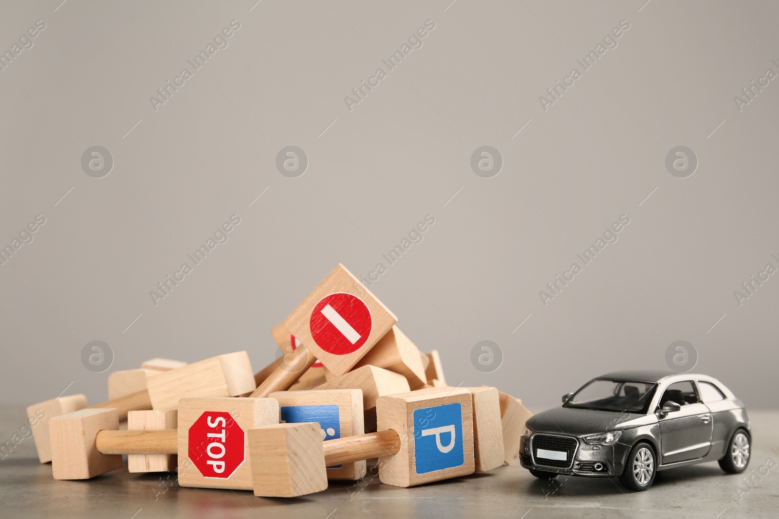 Photo of Many different miniature road signs and car on grey table, space for text. Driving school