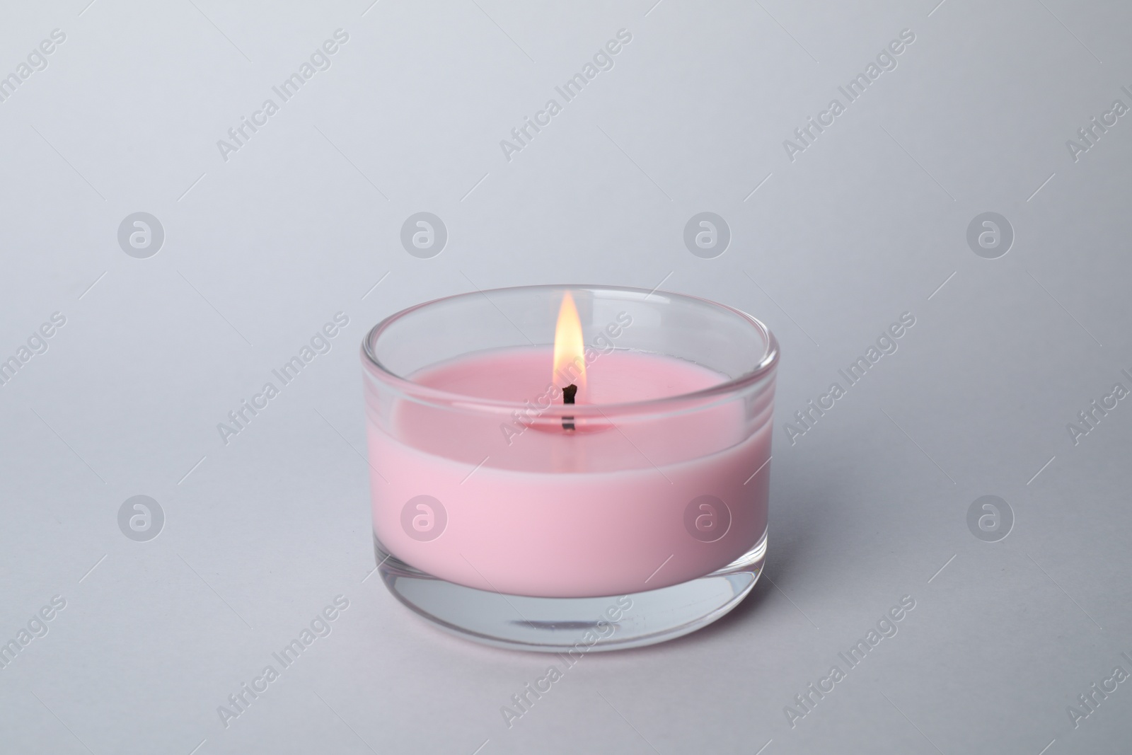 Photo of Burning candle in glass holder on light grey background
