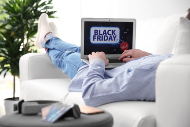 Photo of Man shopping online using laptop on couch at home, closeup. Black Friday Sale