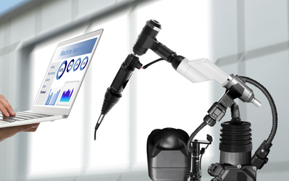 Image of Engineer controlling electronic laboratory robot manipulator with laptop indoors, closeup. Machine learning