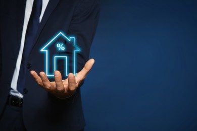 Image of Mortgage rate. Man holding illustration of house with percent sign on dark blue background, closeup. Space for text