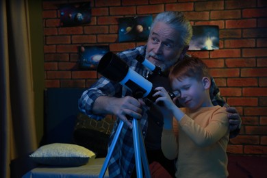 Little boy with his grandfather looking at stars through telescope in room